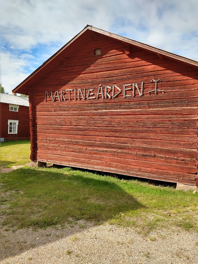 Bild som visar gaveln av ett rödmålat timrat uthus med texten Martingården